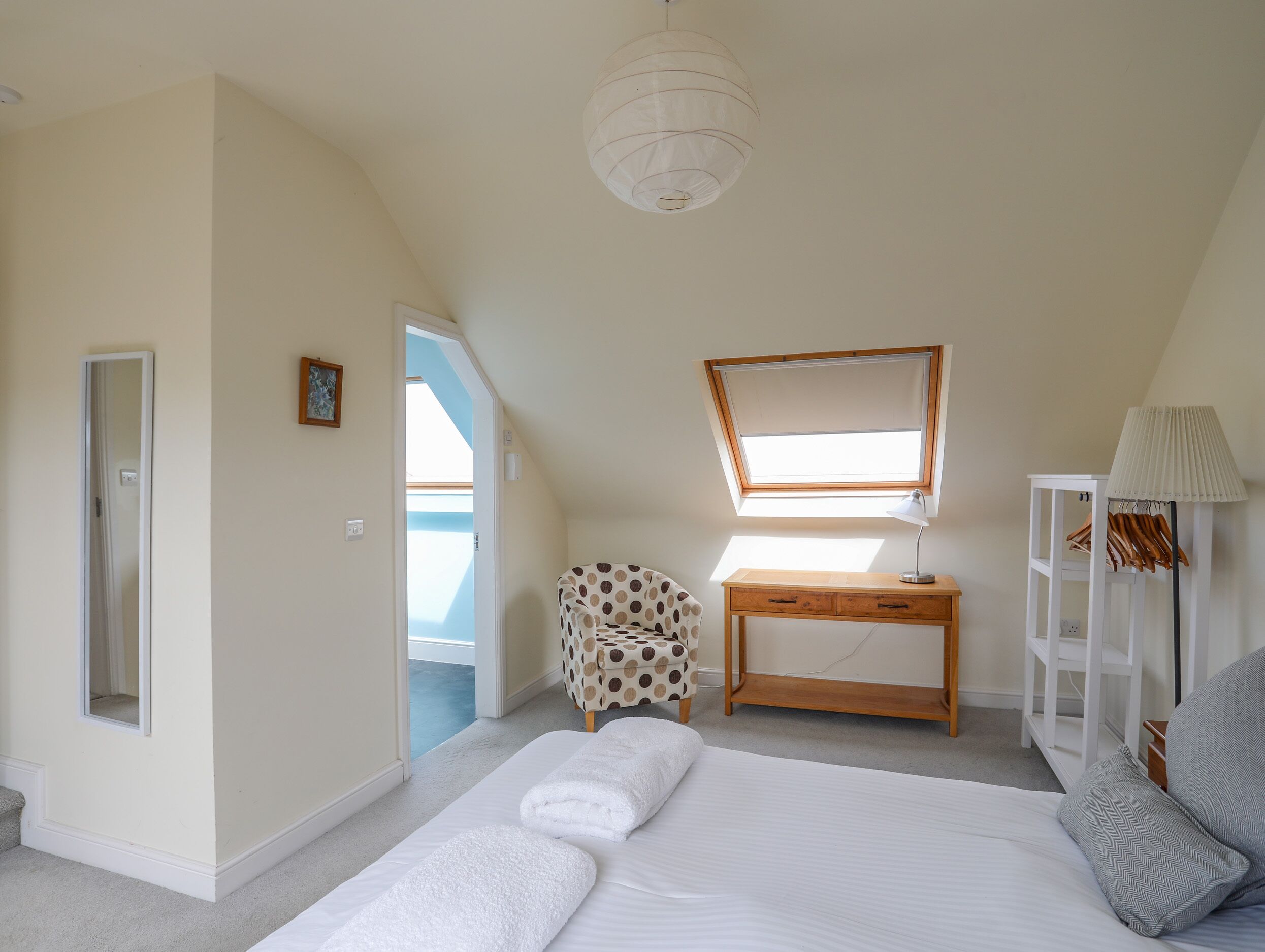 Een slaapkamer met een bed, een bureau, een stoel, een spiegel en een lamp.