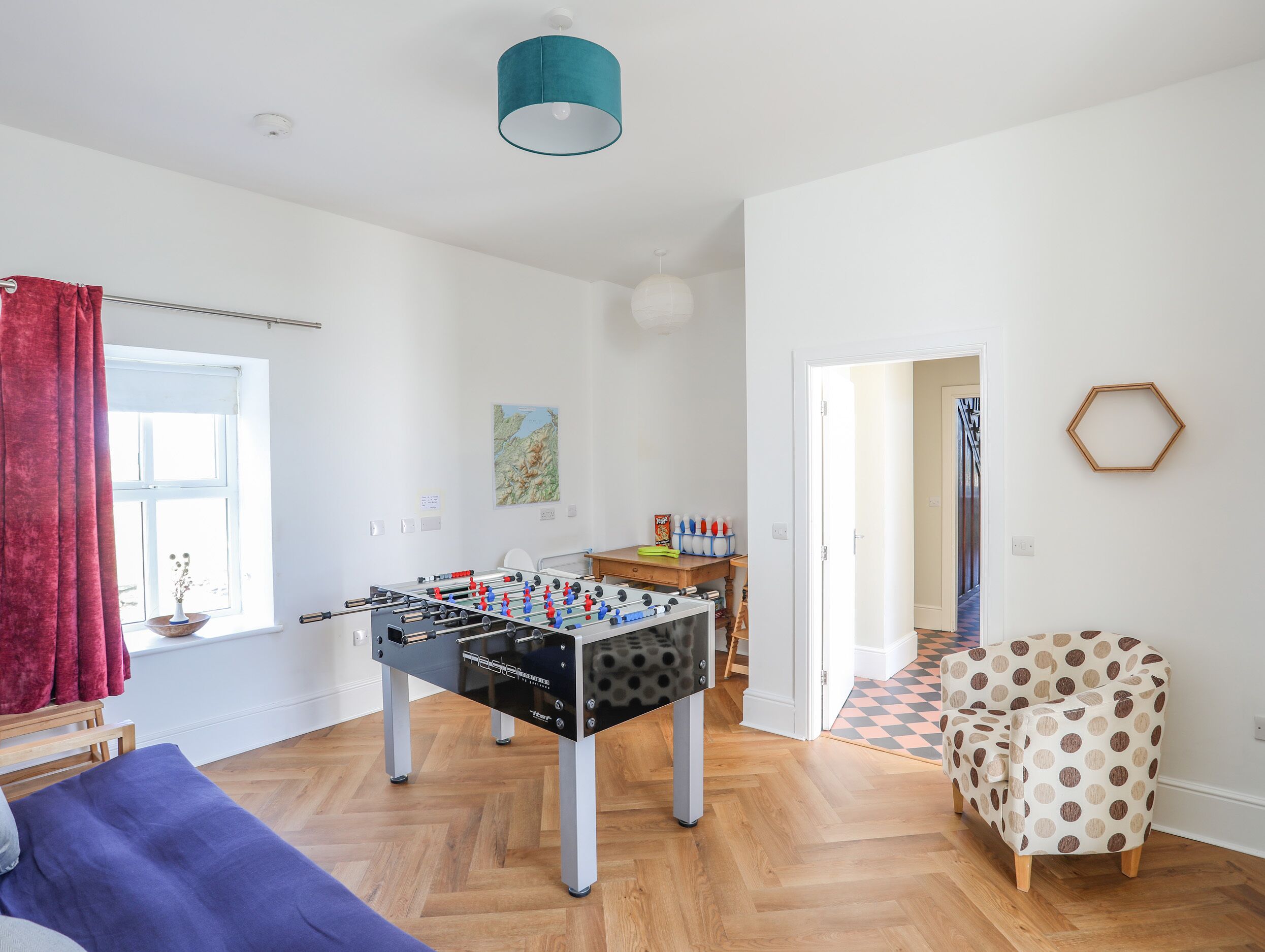 A room with a foosball table, a wooden coffee table, a polka dot chair, and a hexagonal wall decoration.