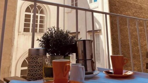 A balcony with a table set for two, overlooking a building with arched windows and a chimney. - PONENTINO 🍾2 Luxury apartments (Trieste)