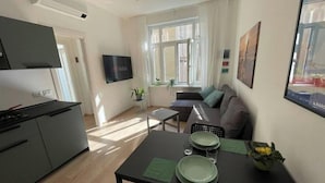 A modern living room with a sofa, a dining table set for two, and a kitchen area with a stove. - PONENTINO 🍾2 Luxury apartments (Trieste)