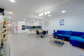 Una sala de estar moderna con un sofá azul, un comedor con una mesa redonda y una cocina con armarios blancos.