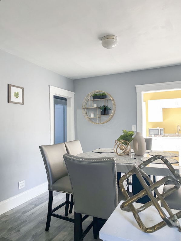 A dining area with a white table, two grey chairs, a decorative wall shelf, and a door leading to another room.