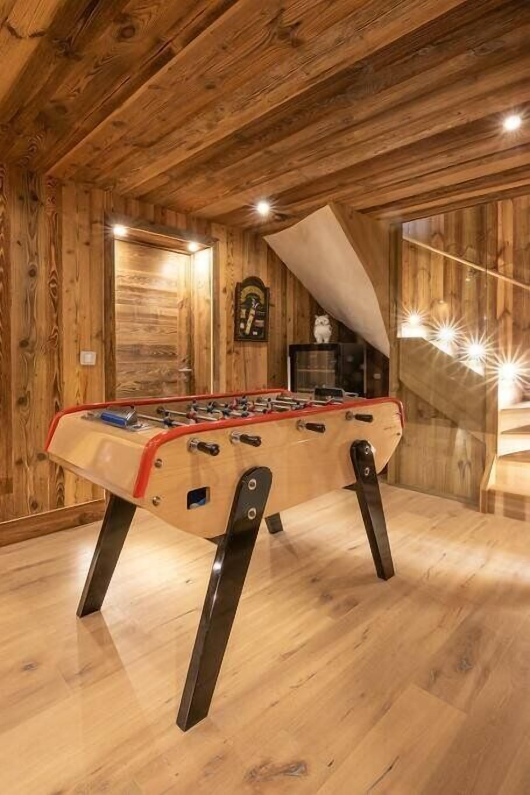 Una habitación con suelo de madera, una mesa de fútbol de mesa, un reloj en la pared y una escalera con techo inclinado.