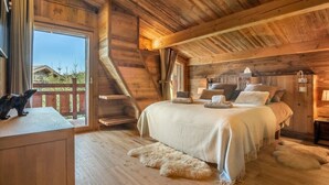 Ein gemütliches Schlafzimmer in einer Holzhütte mit einem großen Bett, einem Holztisch und einem Fenster mit Blick auf einen eingezäunten Bereich.
