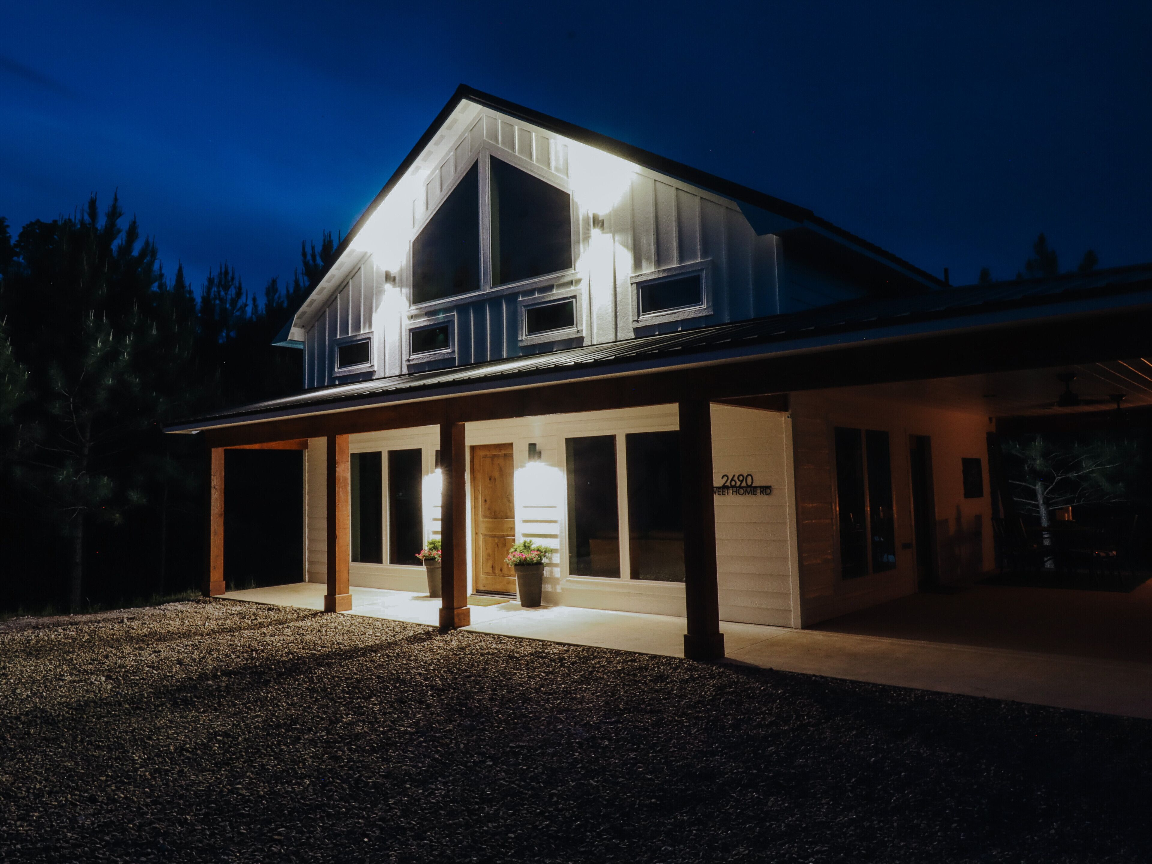 Een modern huis met twee verdiepingen, een overdekte veranda, grote ramen en een goed verlichte ingang.
