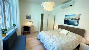 A bedroom with a bed, bedside table, lamp, and a window with a plant. - NEVERIN 🍾3 Luxury apartments (Trieste)