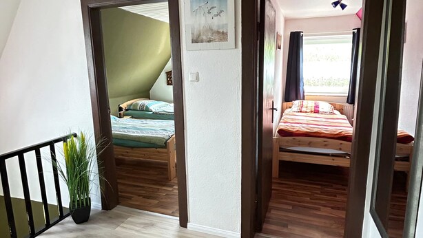 A room with a wooden floor, a bed with a red blanket, a ceiling fan, and a window with curtains. - Vacation apartment on the Elbe-Lübeck Canal. Ideal for cycling tours. (23919 Berkenthin)