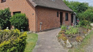 A brick house with a sloped roof, a paved driveway, and a garden with various plants and a small pond. - Vacation apartment on the Elbe-Lübeck Canal. Ideal for cycling tours. (23919 Berkenthin)