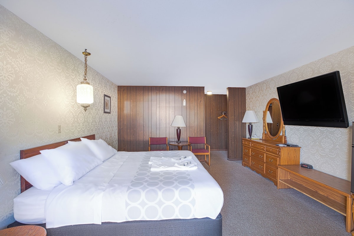 Ein Hotelzimmer mit einem großen Bett, einem hölzernen Schminktisch, einem Flachbildfernseher und einem Schreibtisch mit Stuhl.