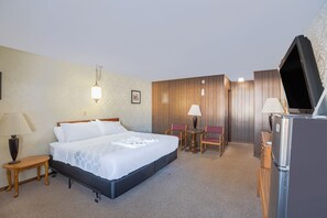 Une chambre d’hôtel équipée d’un lit, d’un bureau, d’une chaise, d’une lampe et d’un réfrigérateur.