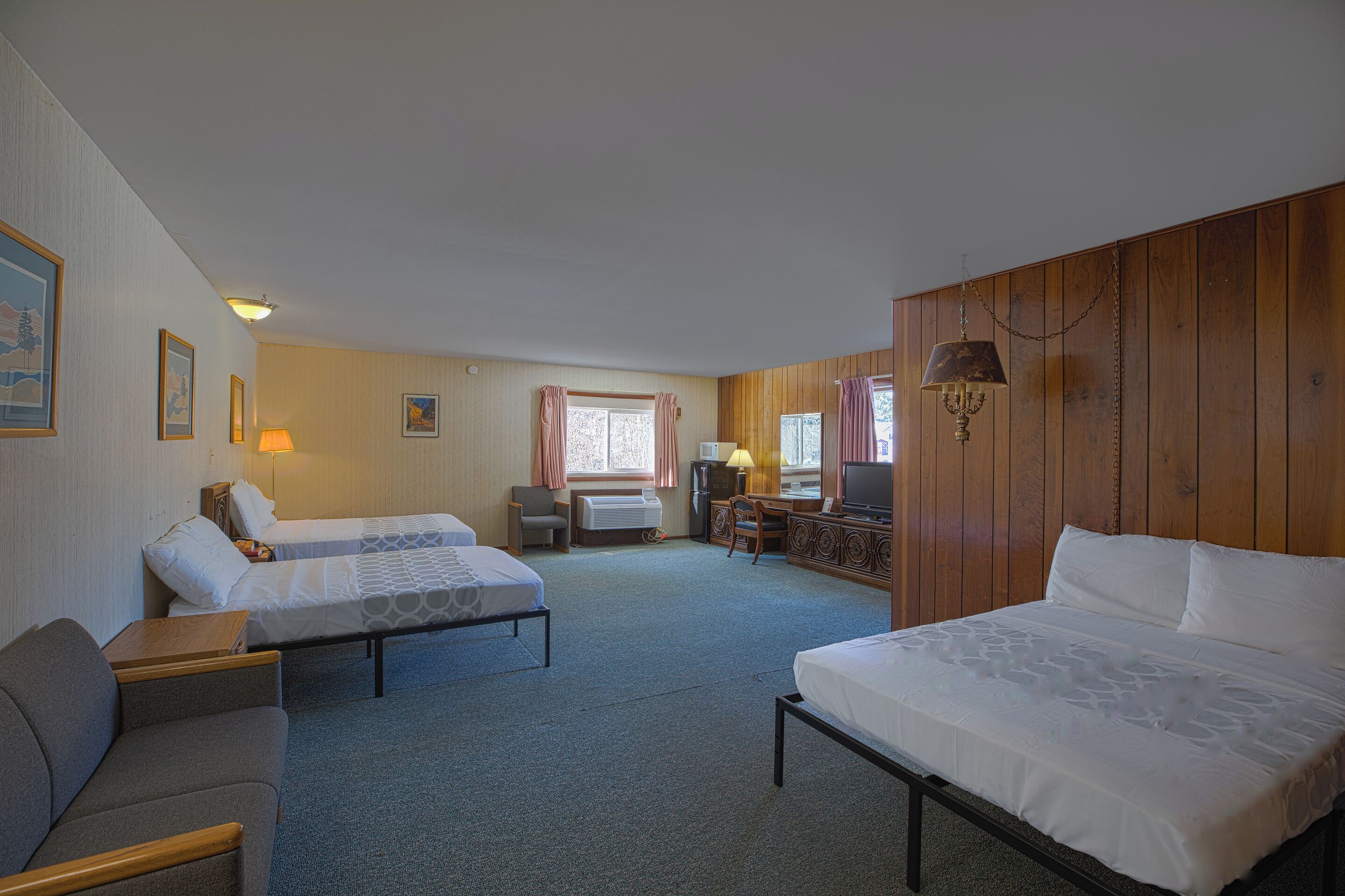 A hotel room with two single beds, a sofa, a desk with a chair, and a television.