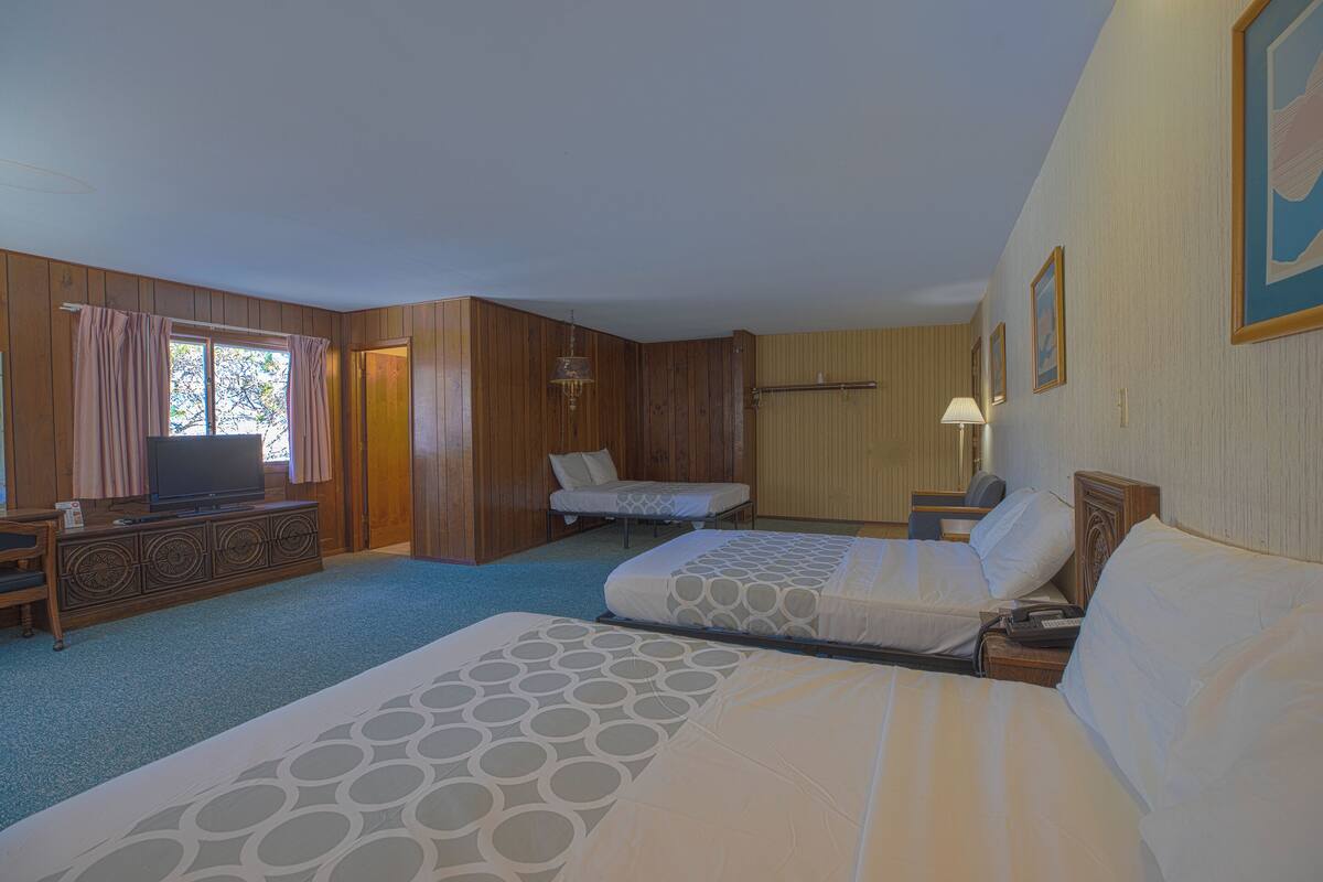 Ein Hotelzimmer mit zwei Betten, einem Fernseher, einem Schreibtisch und einem Fenster mit Vorhängen.