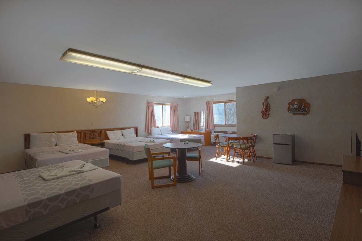 Ein Hotelzimmer mit zwei Einzelbetten, einem kleinen Tisch, einem Stuhl, einem Schreibtisch und einem Kühlschrank.