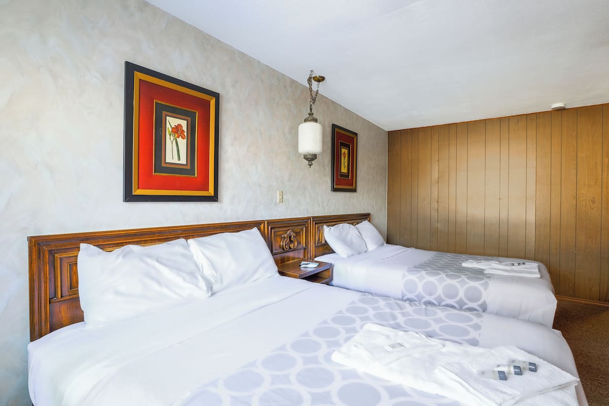 Ein Hotelzimmer mit zwei Betten, einem hölzernen Kopfteil, einem Nachttisch und zwei gerahmten Bildern an der Wand.