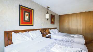 Une chambre d’hôtel avec deux lits, une tête de lit en bois, une table de chevet et deux tableaux encadrés au mur.