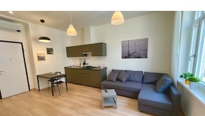 Ein modernes Wohnzimmer mit grauem Sofa, einem kleinen Tisch und einer Küchenzeile mit Schränken und einem Esstisch.