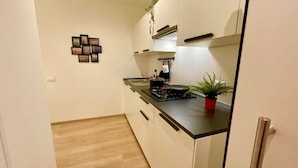 Eine kleine Küche mit schwarzem Arbeitsplatz, weißen Schränken, einem Kochfeld und einem Blumentopf.
