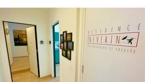 Ein Flur mit einer Tür zu einem Zimmer, einer Wand mit gerahmten Bildern und einem Schild mit der Aufschrift 'RESIDENCE NOVERIN VIA VALDERIVO 21 TRIESTE'.