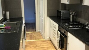 A modern kitchen with a microwave, stove, and oven. There is a wooden floor and a door leading to another room. - Lovely 4-bed House in Anfield all En-suite, (Liverpool)