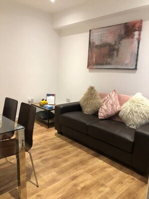 A modern living room with a black leather sofa, a glass dining table, and a wooden floor.