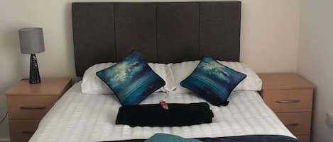 Una cama bien hecha con un edredón azul oscuro, dos almohadas iguales y una almohada turquesa.