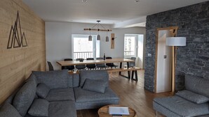 Uma sala de estar moderna com sofás cinzentos, uma mesa de centro de madeira e uma área de jantar com uma mesa e cadeiras de madeira.