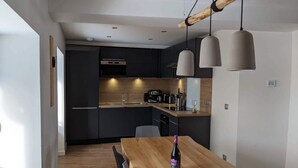 Uma cozinha moderna com armários escuros, uma mesa de jantar de madeira e luminárias pendentes.