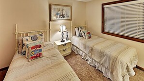 A bedroom with two single beds, a nightstand with a lamp, a framed picture above the beds, and a window with blinds. - 2 Bedroom Condo at Myrtle beach (Myrtle Beach)