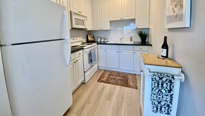 Una cocina con gabinetes blancos, un refrigerador blanco, un microondas, un horno, un fregadero y una encimera de madera.