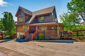 A two-story log cabin with a porch, a satellite dish, and a small garden. - Lux Lodge! Pool-Sauna-HotTub-Game-Pet Frndly (Sevierville)