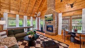 A log cabin interior with a fireplace, wooden ceiling, and a dining area. - Lux Lodge! Pool-Sauna-HotTub-Game-Pet Frndly (Sevierville)