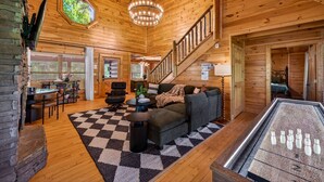 A log cabin interior with a checkered rug, a sofa, a dining area, and a staircase. - Lux Lodge! Pool-Sauna-HotTub-Game-Pet Frndly (Sevierville)