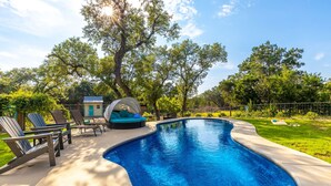 A swimming pool with lounge chairs and a hot tub in a backyard setting.