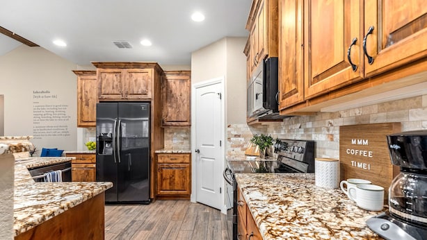 A kitchen with wooden cabinets, a black refrigerator, a coffee maker, and a sign that reads "MMM COFFEE TIME!".
