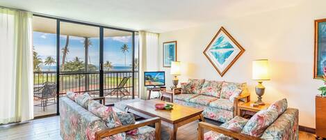 Ein großzügiges Wohnzimmer mit Balkon und Blick auf eine schöne Landschaft, ausgestattet mit Sofas mit Blumenmuster und einem Holztisch.