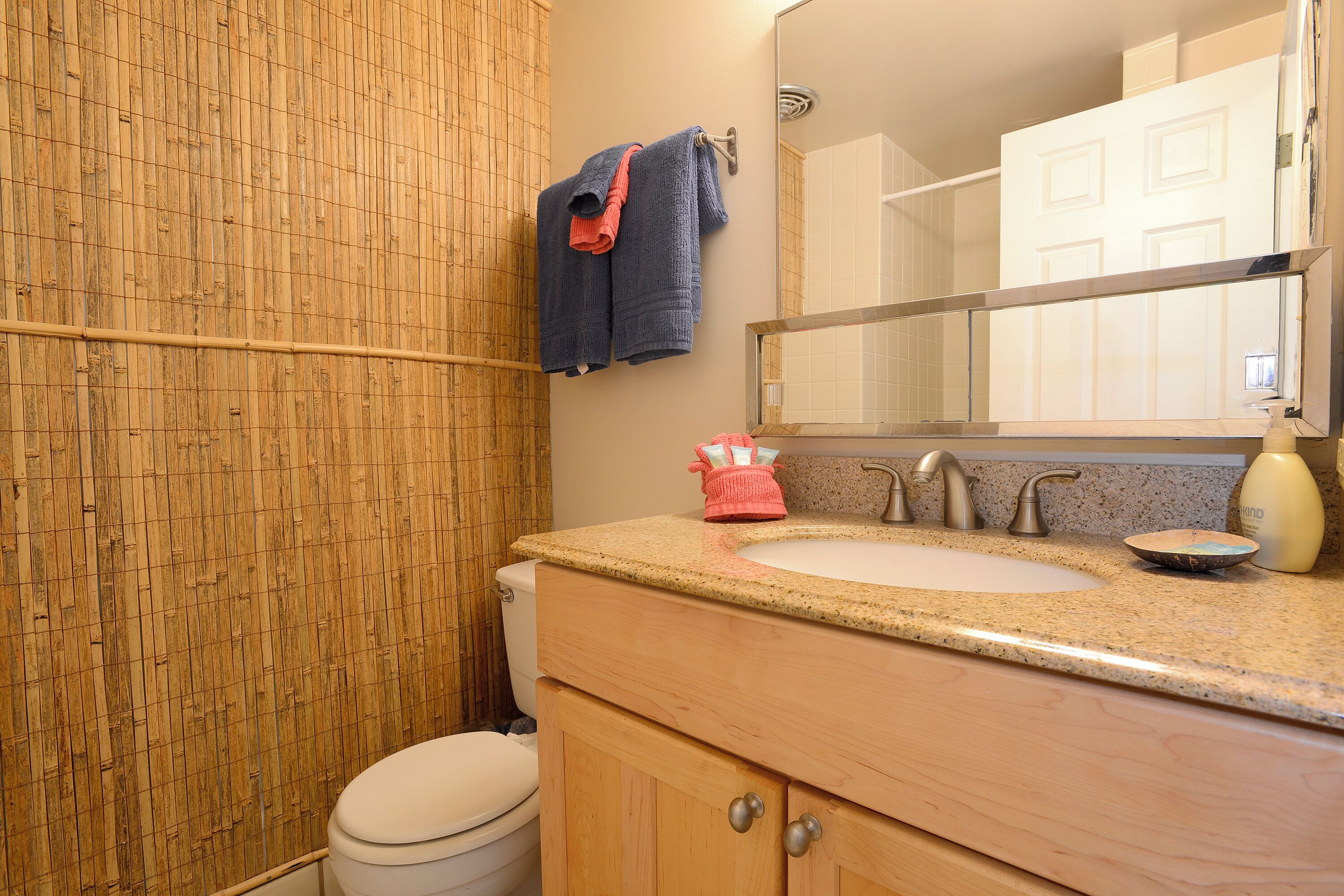 A bathroom with a bamboo shower curtain, a toilet, a sink with a mirror above it, and a towel rack with towels.
