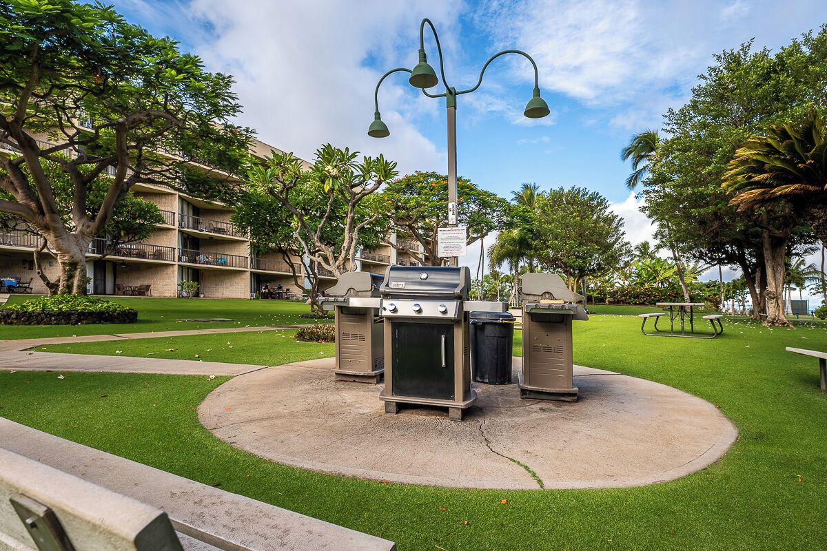 An outdoor barbecue area with a grill, trash bins, and a street lamp.