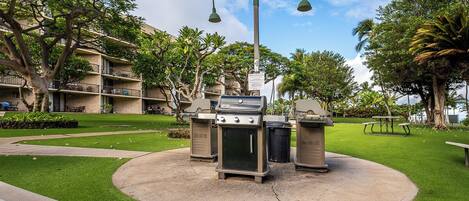 An outdoor barbecue area with a grill, trash bins, and a street lamp.