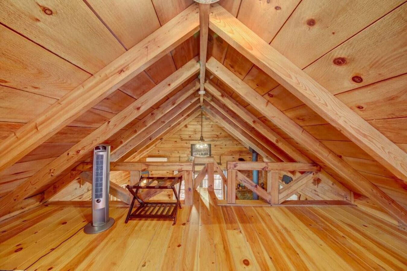 Quarto de sótão em madeira com teto inclinado, aquecimento central e uma pequena mesa.