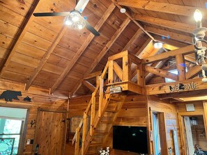 Cozy cabin interior with a wooden staircase, ceiling fan, and wall-mounted TV.