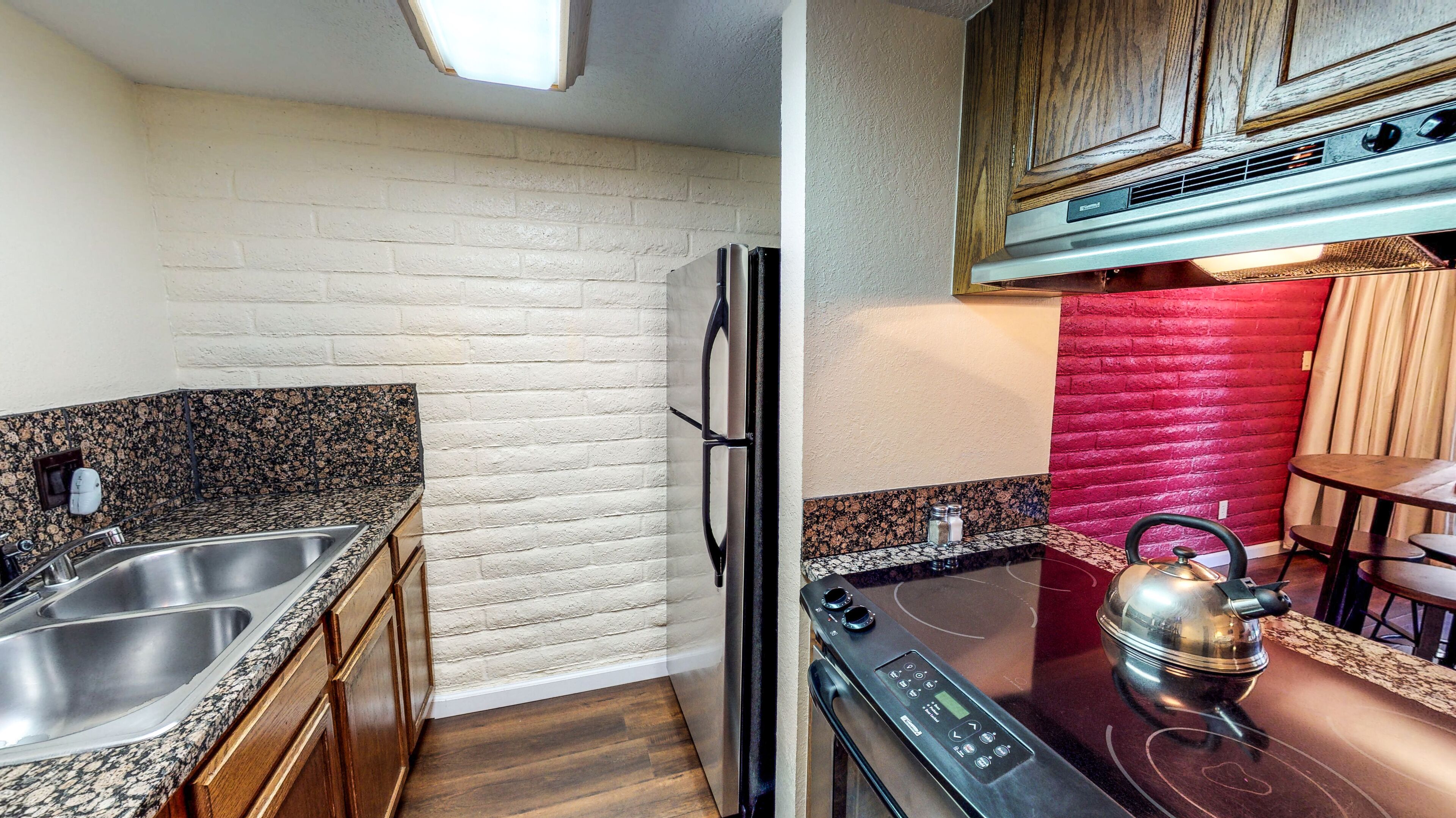 A compact kitchen with granite countertops, a stainless steel sink, a refrigerator, and a stove.