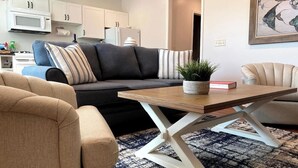 A living room with a sofa, a coffee table, and a kitchen in the background.