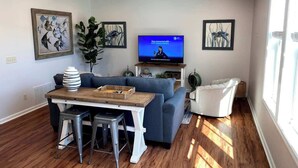 A living room with a TV, a sofa, a dining table with stools, and artwork on the walls.