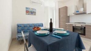 A dining area with a table set for four, a blue sofa, and a kitchen with modern appliances. - Villette Girovagando - Superior by BarbarHouse (Torre dell'Orso)