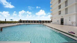 Una piscina con agua azul cristalina, un edificio con numerosas ventanas y un cielo despejado.