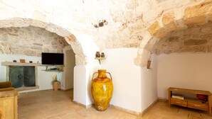 Une pièce aux murs de pierre, avec une télévision, un grand vase et un banc en bois.