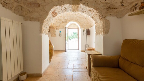 Une pièce dotée d’un plafond en pierre, d’un banc en bois, d’un radiateur et d’une porte-fenêtre donnant sur un espace extérieur.