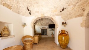Un couloir étroit aux murs de pierre, meublé de mobilier en osier et agrémenté d’un grand vase.