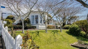 Een wit huis met een groot gazon, een witte schutting en een verzorgde tuin.