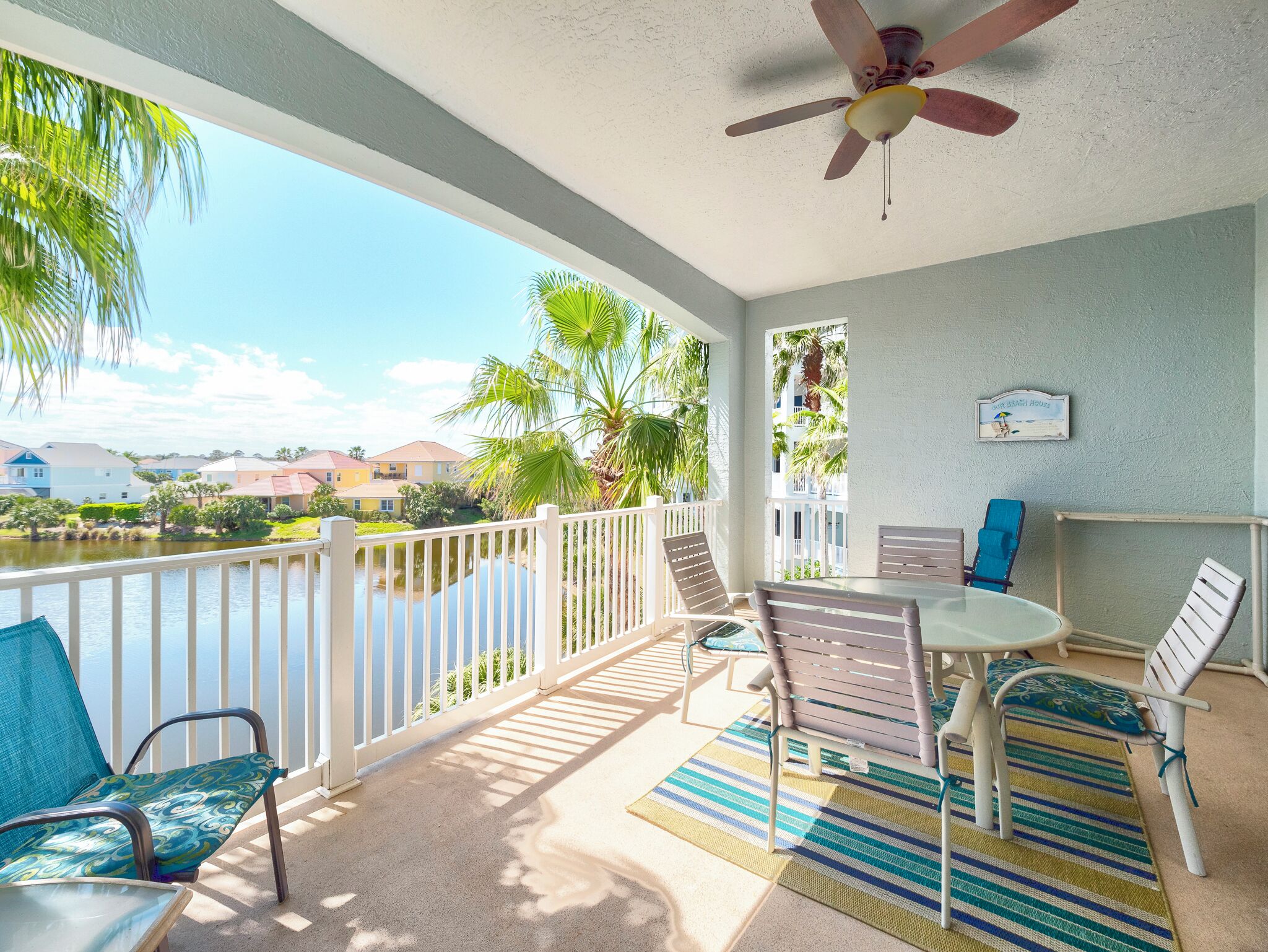 A balcony with a view of a lake and houses, a ceiling fan, and a table with chairs.